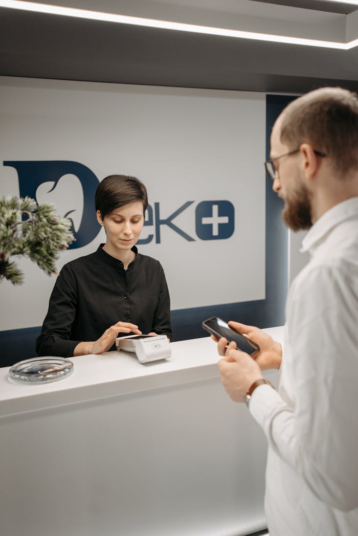 services-01 Customer making a cashless payment at a clinic reception using a smartphone and a wireless terminal.