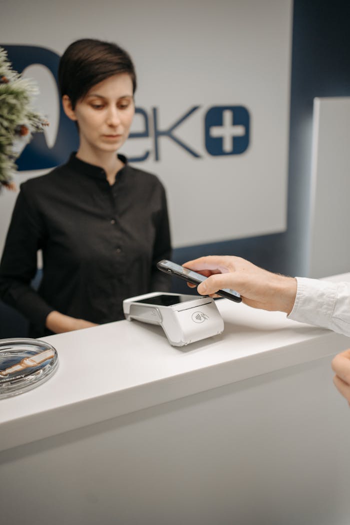 about-bg A woman witnesses a customer making a contactless payment using a smartphone at a service counter.