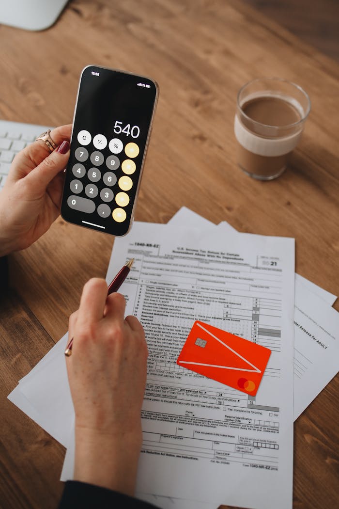 services-04 A person uses a smartphone calculator over tax documents on a wooden table.
