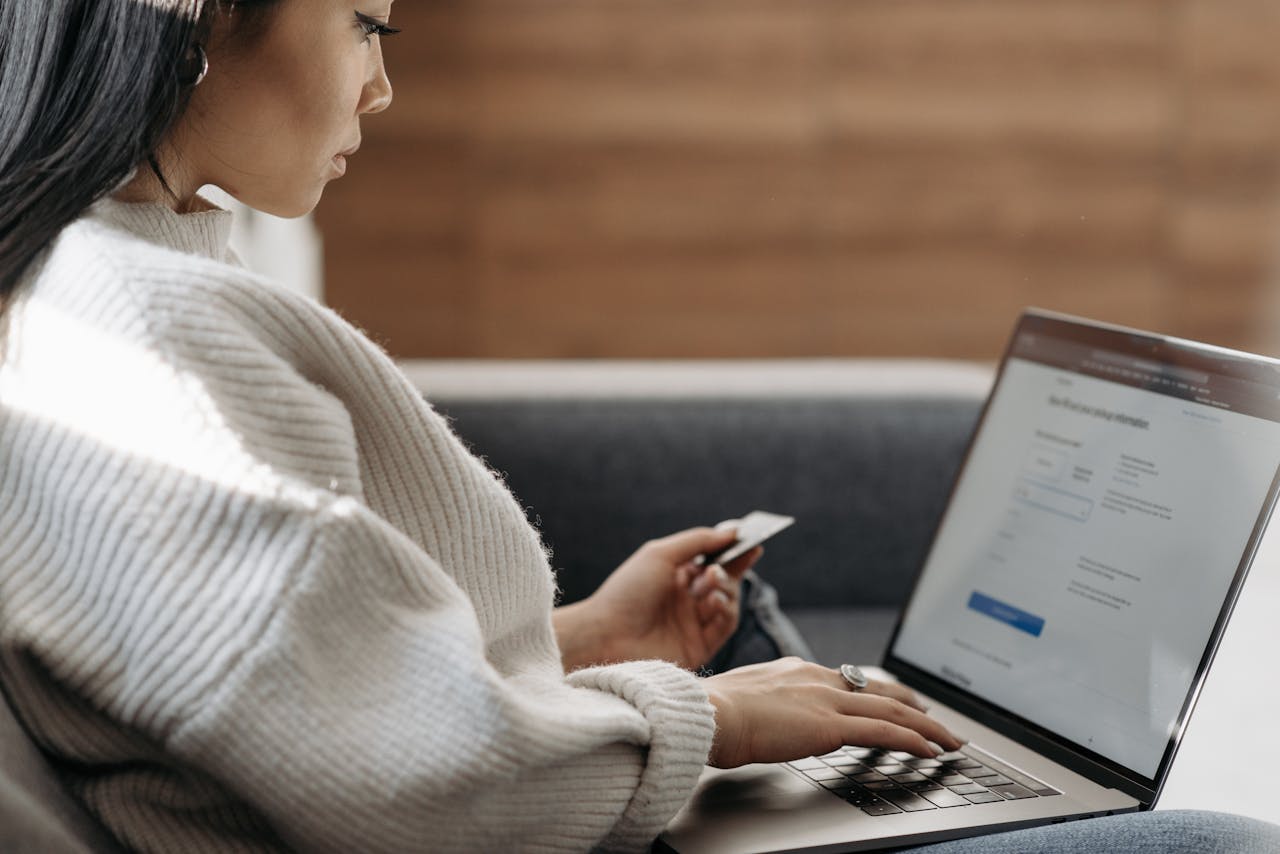 why-choose-us Woman sitting on a couch, shopping online using a laptop and a credit card.