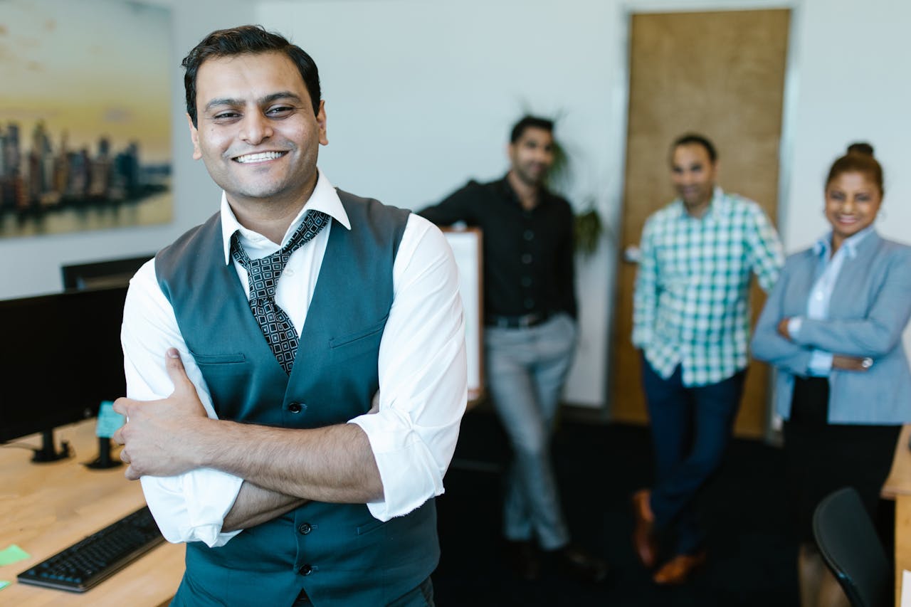 get-in-touch Smiling businessman in a vest with diverse team posing in modern office setting.